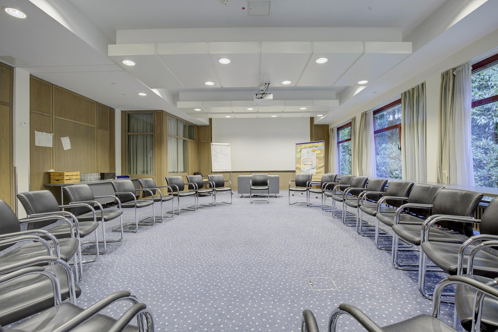 Une salle de conférence équipée d’une longue table, de chaises, d’un tableau blanc et d’un écran de projection.
