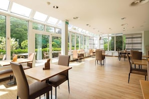 Un espacio interior amplio con varias mesas y sillas, ventanas grandes y vistas a zonas verdes.