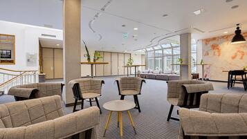 A modern lounge area with seating and tables, large windows, and a decorative wall.