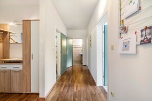 A hallway with wooden flooring, a mirror, a wooden cabinet, and a door leading to a bathroom.