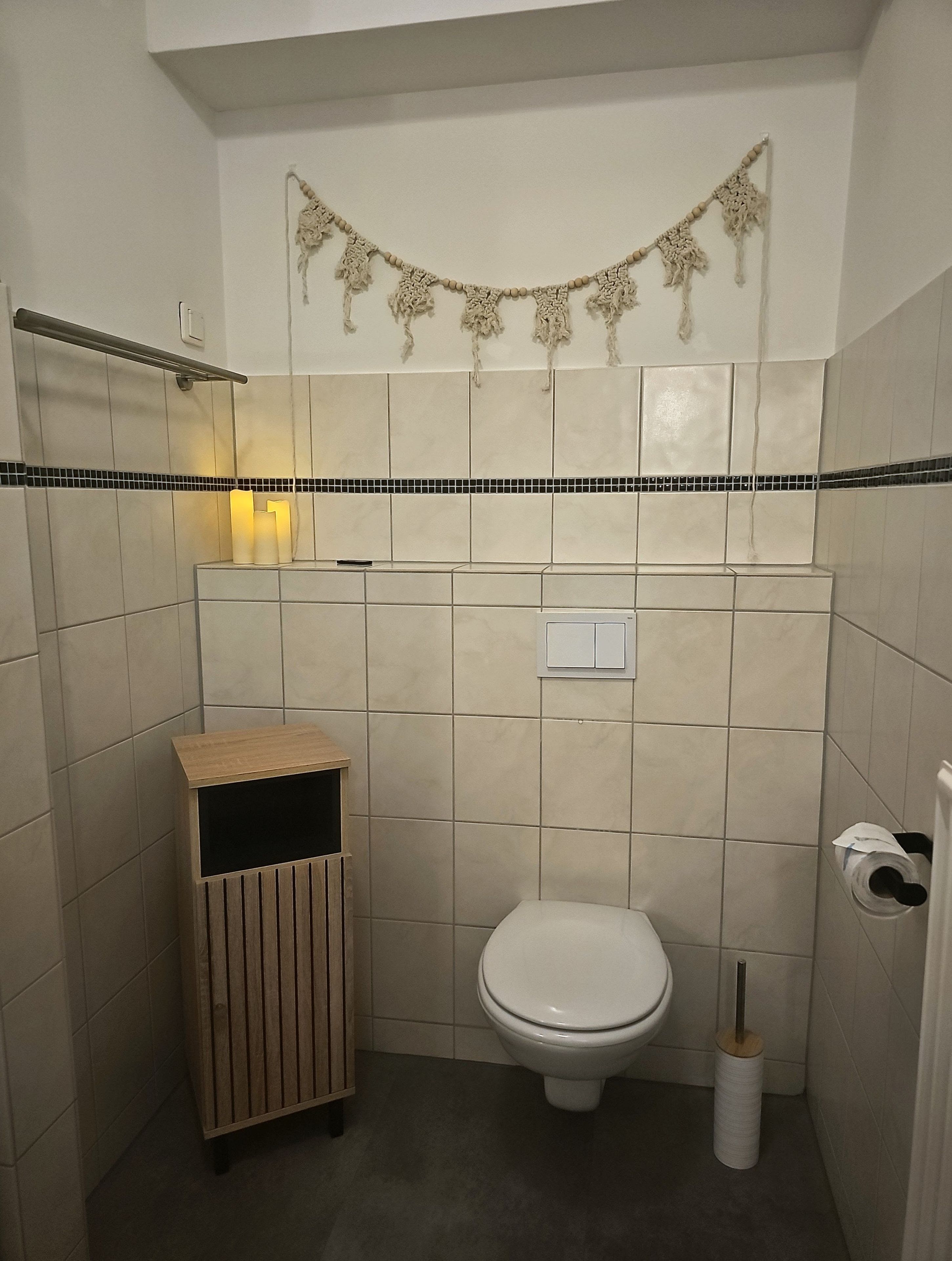 Ein kleines Badezimmer mit Toilette, einem Mülleimer und einem Handtuchhalter an der Wand.