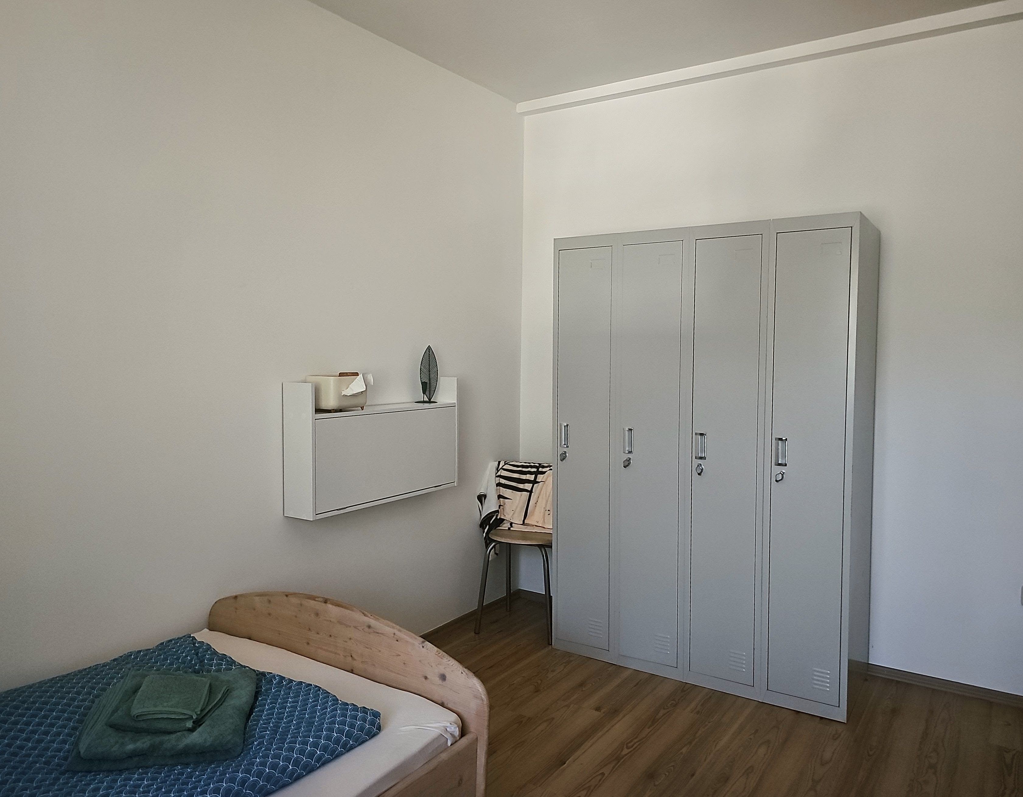 Ein Schlafzimmer mit einem Bett, einem Sessel, einem Kleiderschrank und einem Regal mit Taschentuchbox und Dekoration.