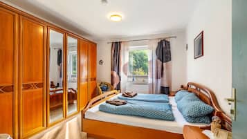 Ein Schlafzimmer mit einem Holzschrank, einem Bett mit gemusterten Betttextilien, einem Fenster mit Vorhängen und einem Nachttisch.