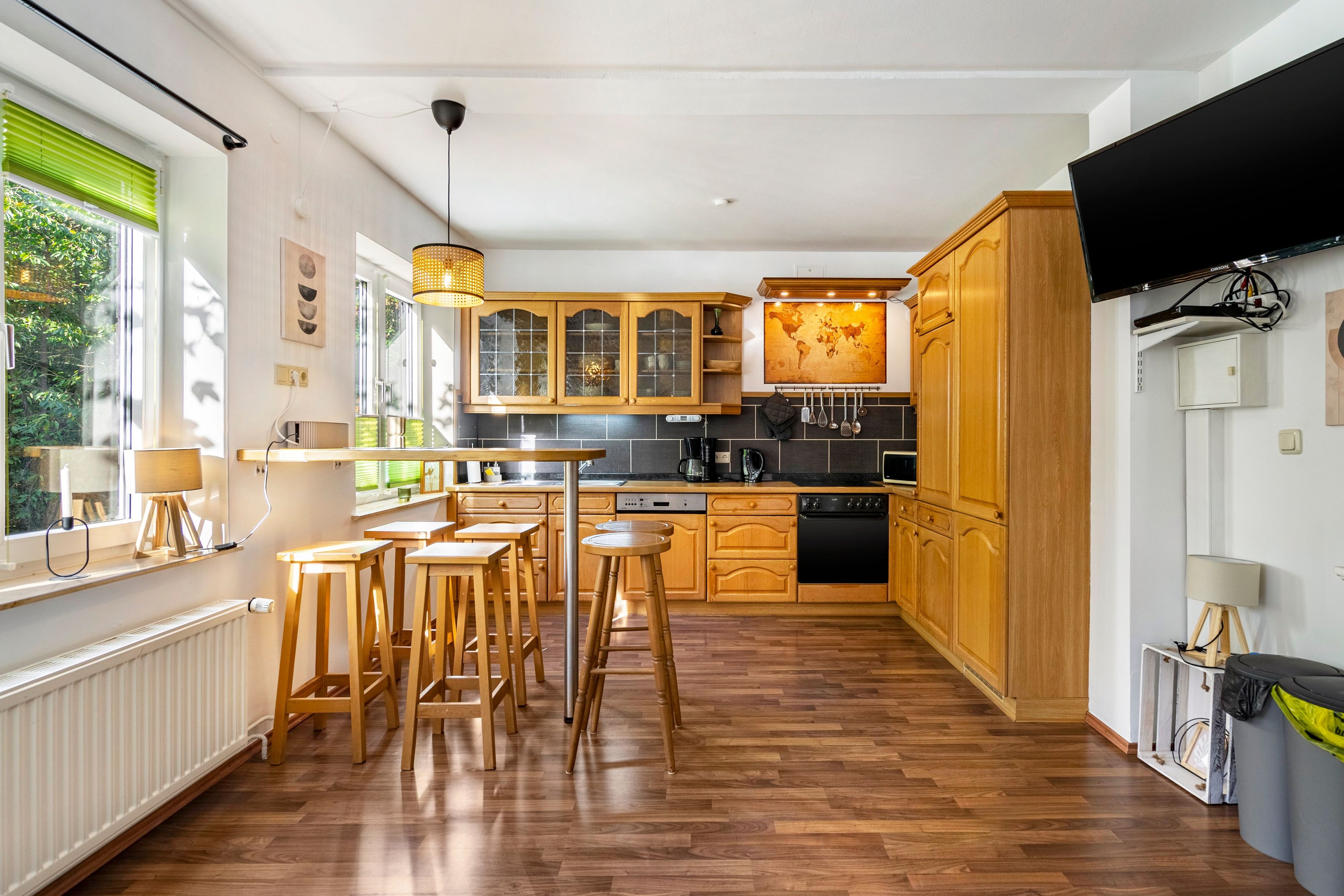 Eine moderne Küche mit Holzausstattung, einem Essbereich mit Hocker und einem großen Fenster, das für natürliches Licht sorgt.