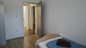 A small, single-bed room with a wooden floor, a white door, and a blue mattress. - Apartment 1 – Schrappmühle with Terrace, Garden, Wi-Fi, and Rural Seclusion (Aerzen)