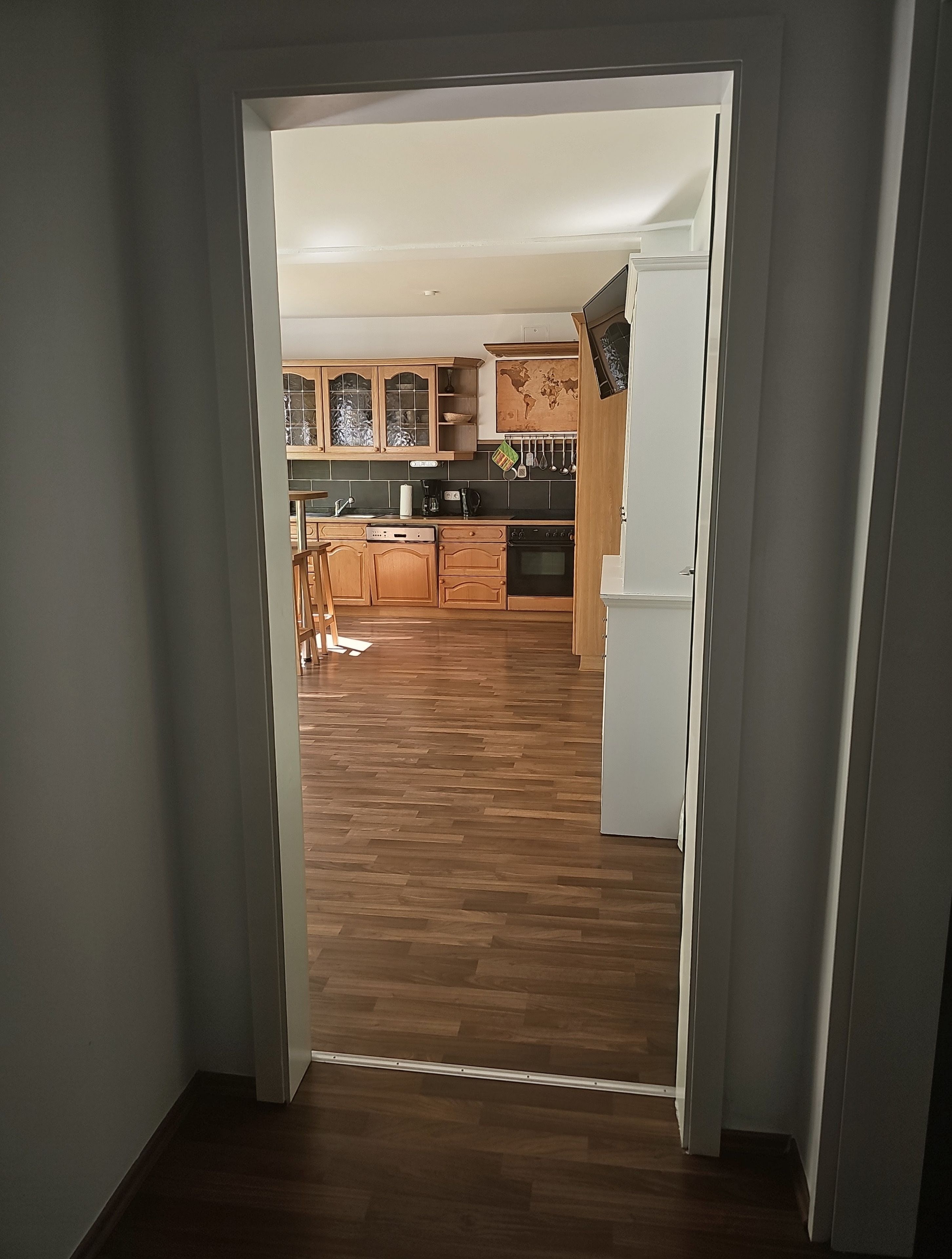 A view through a doorway into a kitchen with wooden cabinets, a stove, and a refrigerator.