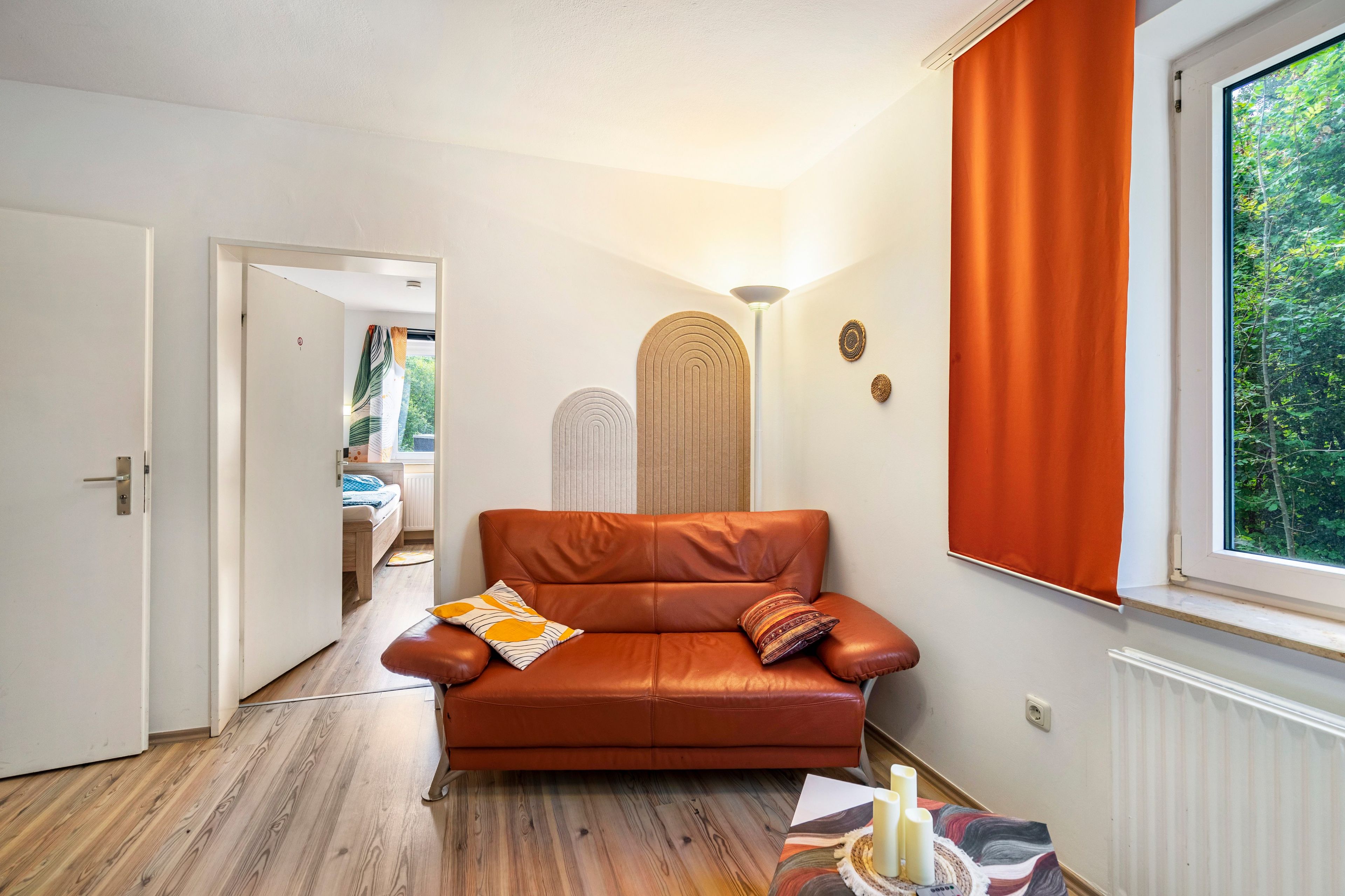 Une pièce chaleureuse avec un canapé en cuir, un plancher en bois, une fenêtre avec des rideaux et une porte donnant sur une autre pièce.
