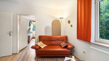 A cozy room with a leather sofa, a wooden floor, a window with curtains, and a door leading to another room.