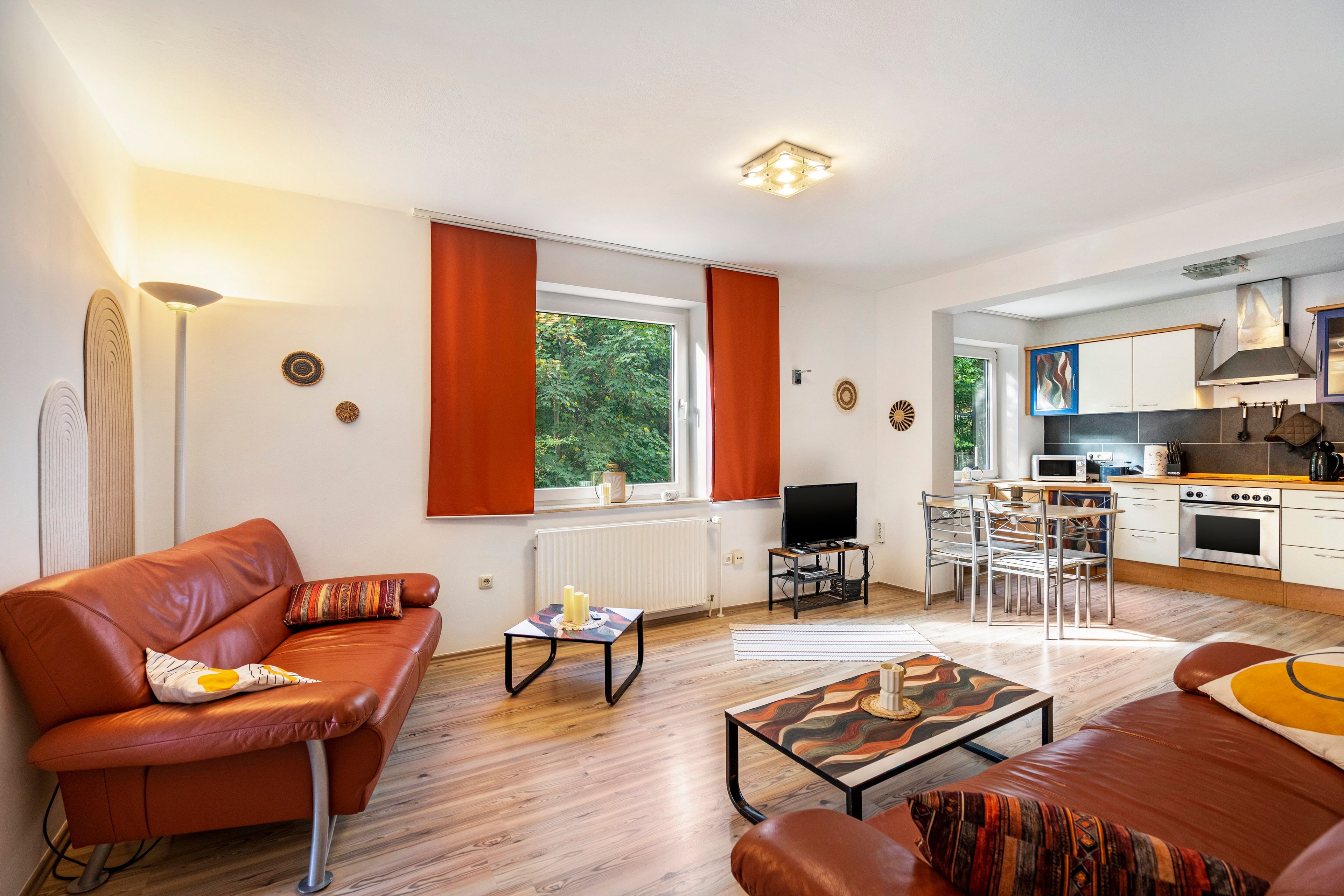 Ein modernes Wohnzimmer mit einer Couch, einem Couchtisch und einem Fernseher. Es gibt eine Küchenzeile mit einer Mikrowelle und einem Herd.