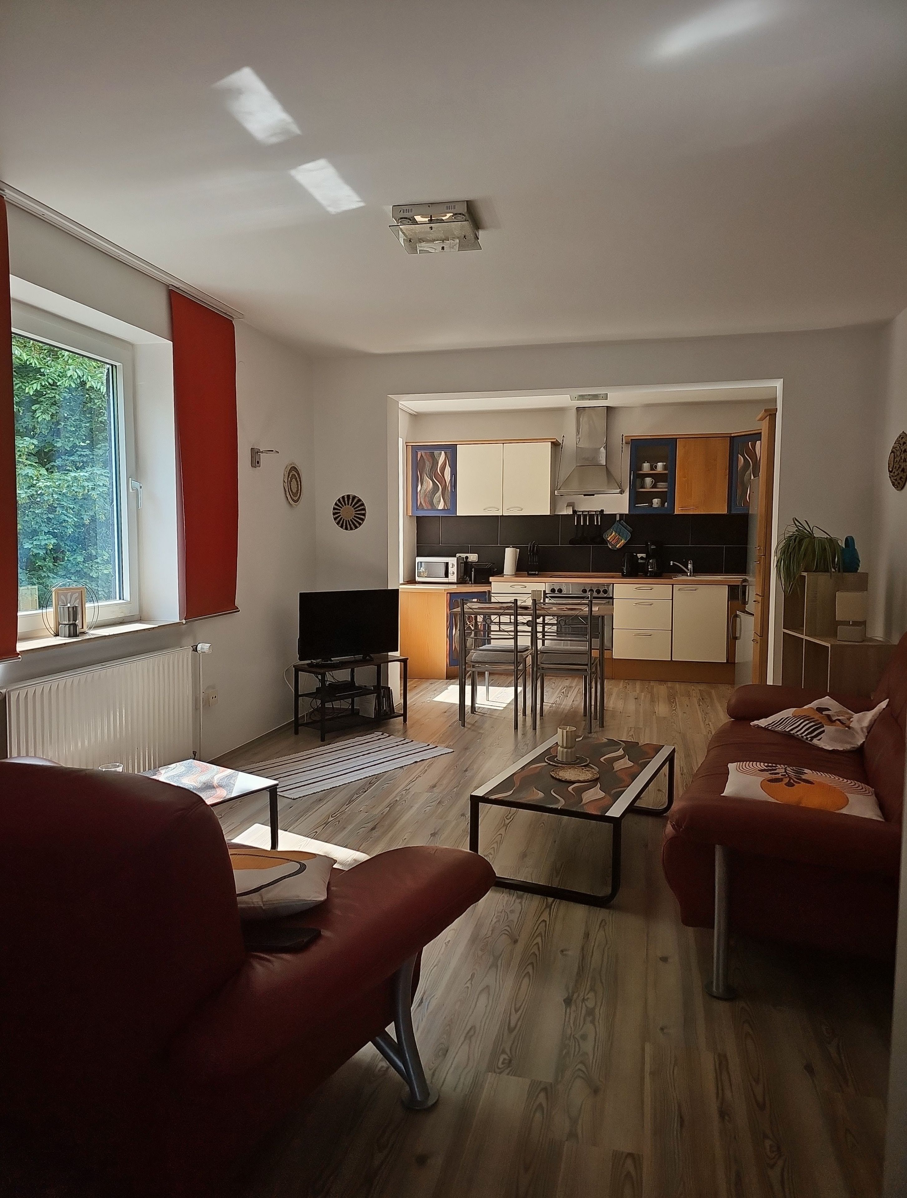 Un salon moderne avec un canapé, une table basse et un téléviseur. Il y a également un coin cuisine avec des placards et une table à manger.