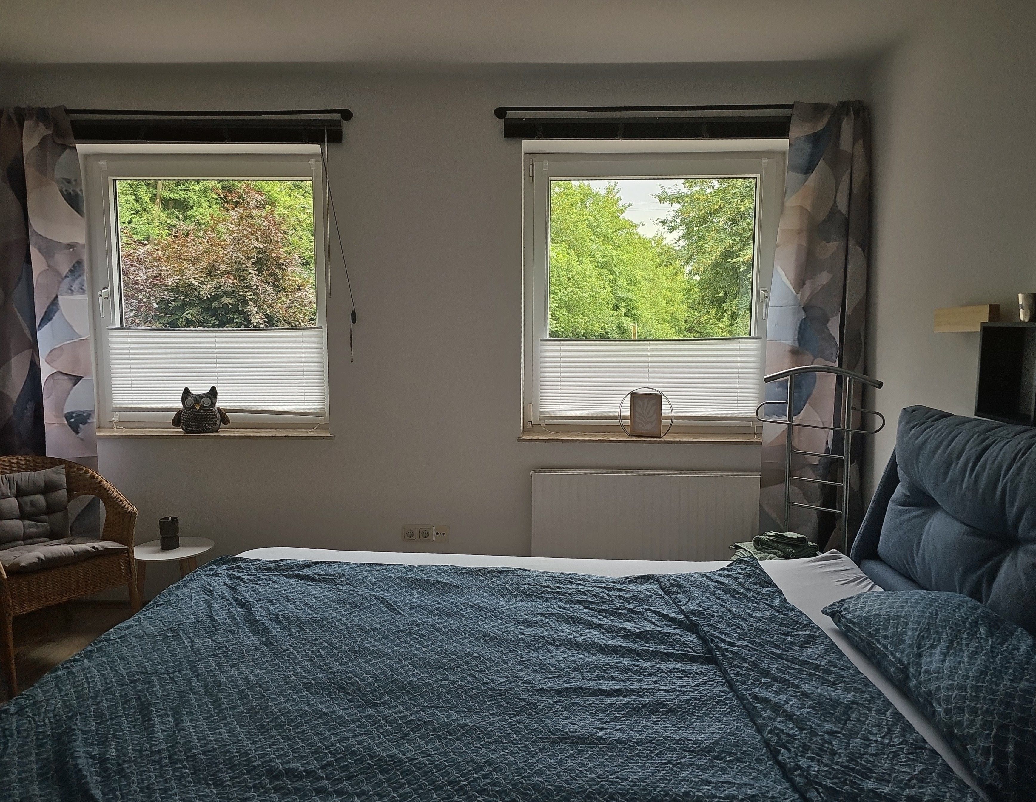 Un dormitorio con dos ventanas, una cama, una silla y un radiador.