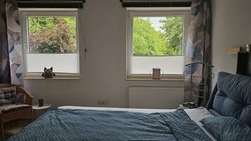 Un dormitorio con dos ventanas, una cama, una silla y un radiador.