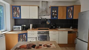 Una cocina moderna con armarios blancos y de madera, horno empotrado, un lavamanos y una mesa de comedor con un mantel individual.