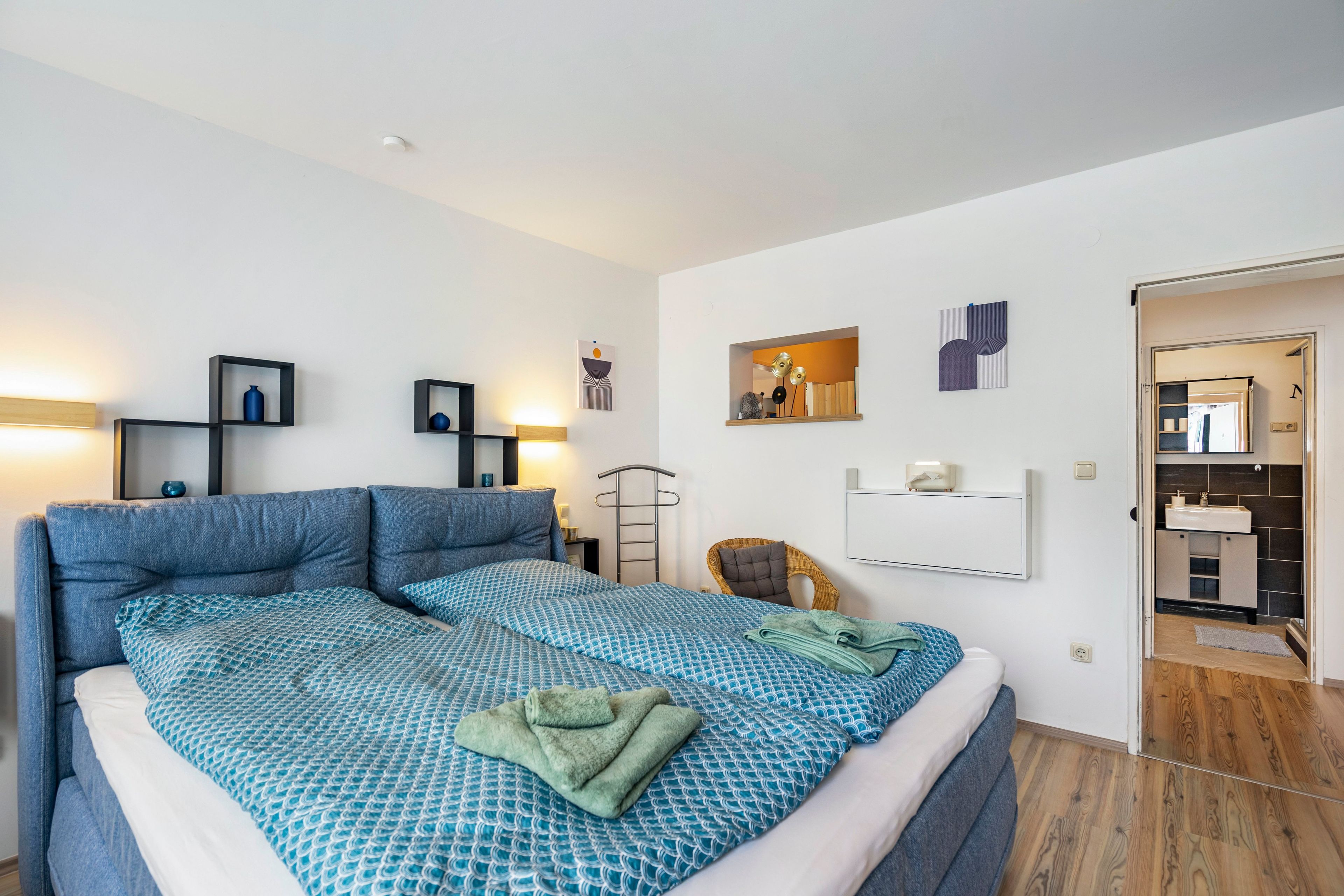 A modern bedroom with a large bed, bedside tables, a wardrobe, and a bathroom visible through an open door.