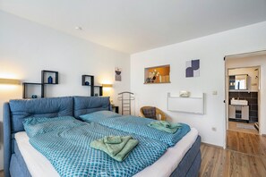 Un dormitorio moderno con una cama grande, mesitas de noche, un armario y un baño visible a través de una puerta abierta.