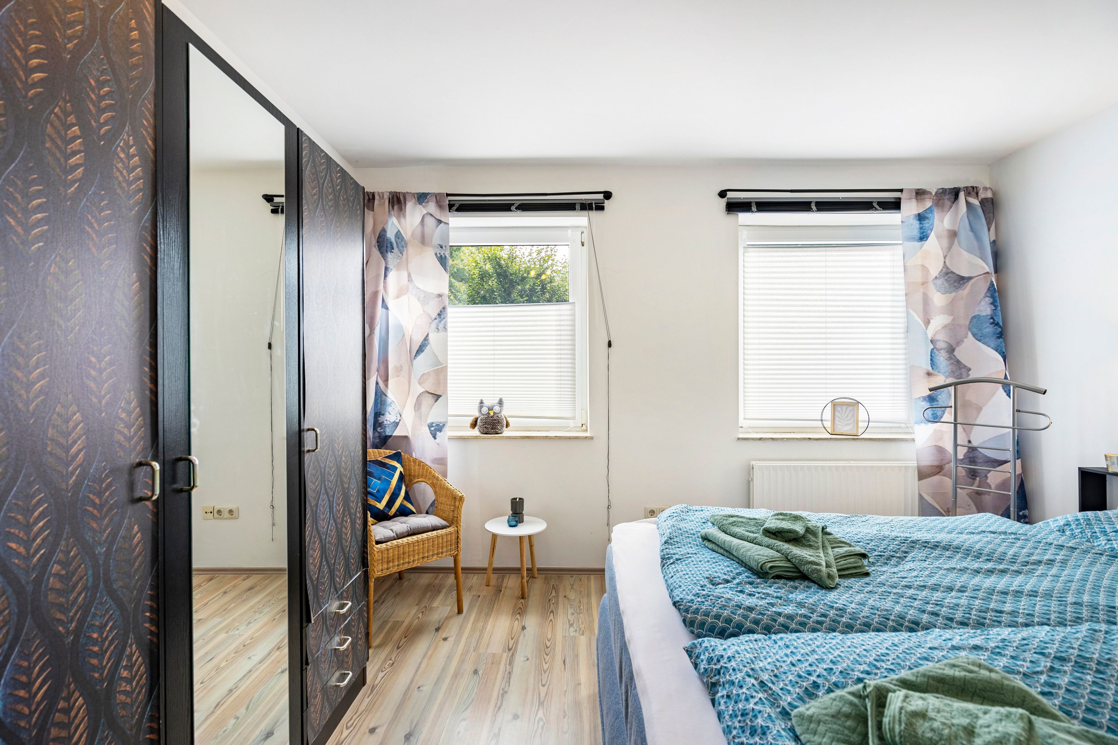 Ein Schlafzimmer mit einem Bett, einem Sessel, einem kleinen Tisch und einem Fenster mit Jalousien.