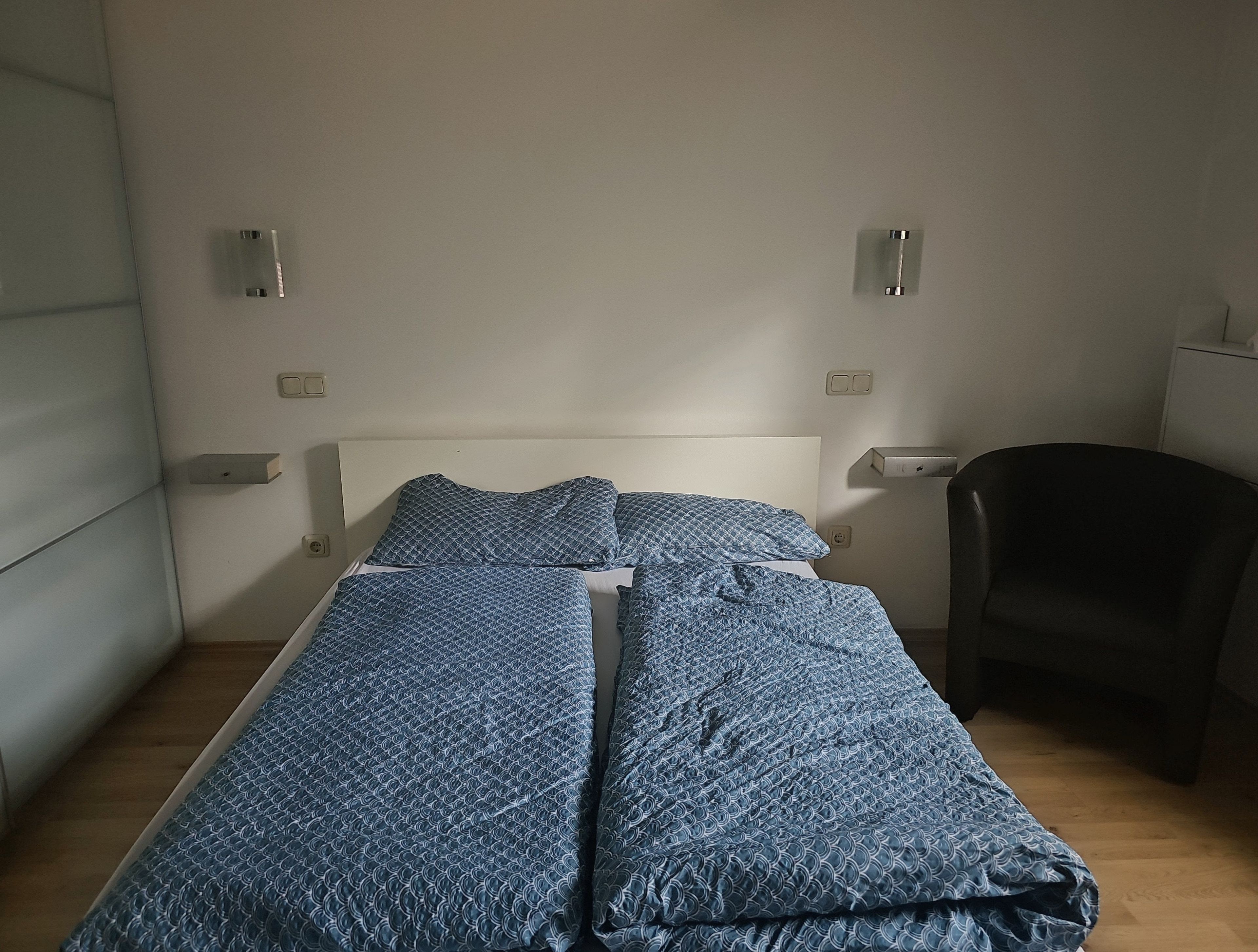 A single bed with a white headboard and blue patterned bedding in a room with a wooden floor.