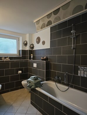 Ein modernes Badezimmer mit Badewanne, Dusche und einem Fenster für natürliches Licht.