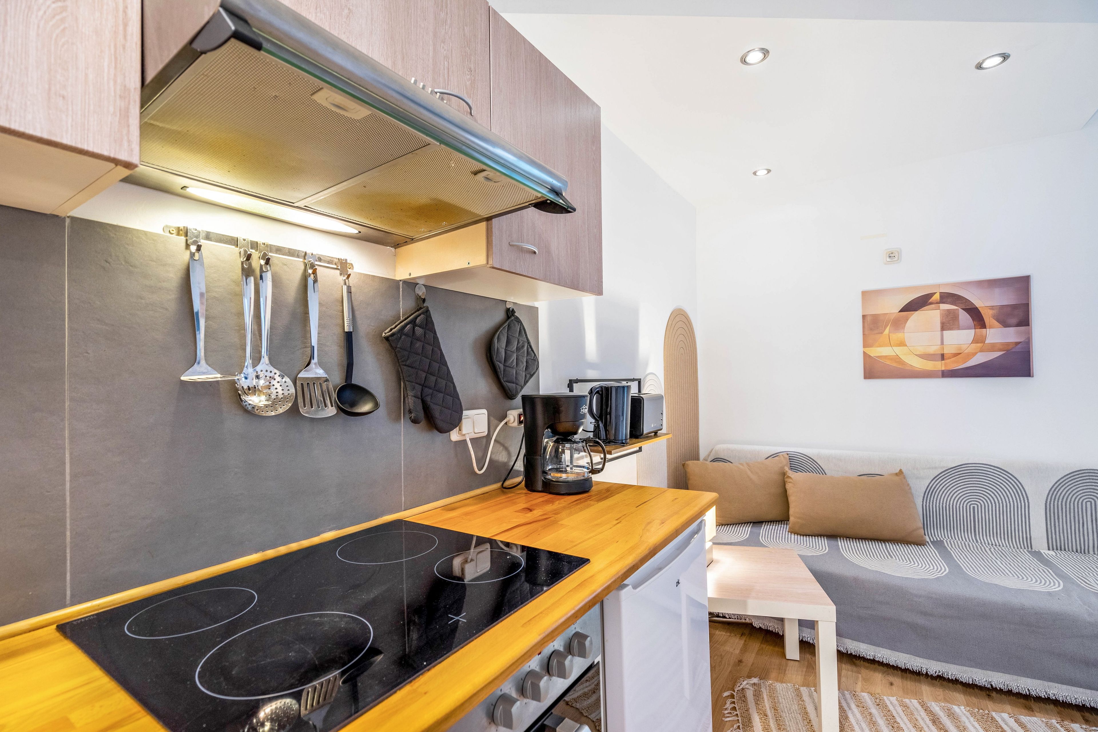 A compact kitchen with a stove, coffee maker, and hanging utensils.