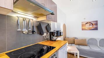 A compact kitchen with a stove, coffee maker, and hanging utensils.
