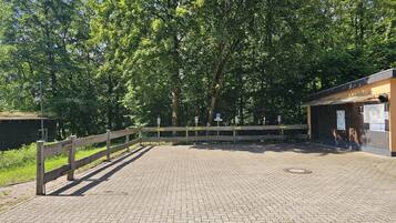 A paved parking area with a wooden fence, a small building with a sign, and trees in the background.