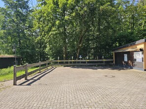 A paved parking area with a wooden fence, a small building with a sign, and trees in the background.