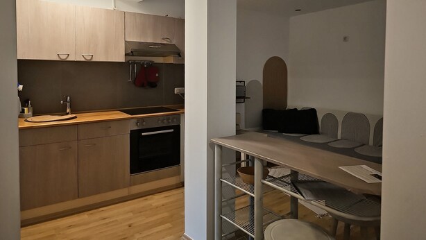Una cocina moderna con armarios de madera, horno empotrado y zona de comedor con mesa y sillas.