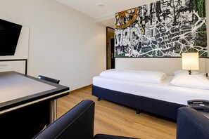 A hotel room with a bed, a desk, a chair, a TV, and a wall art piece. - Seminaris Sunday Hotel Bad Honnef - Standard Single Room (Bad Honnef am Rhein)