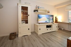A living room with a television on a cabinet, a fireplace, and a window with blinds. - Holiday apartment with 2 bedrooms (Wyk auf Föhr)