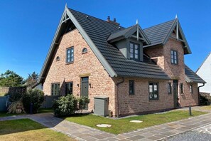 Ein zweistöckiges Ziegelhaus mit einem steilen Satteldach, einer Veranda und einem gepflegten Rasen.