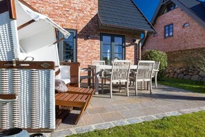Ein Backsteinhaus mit einer Terrasse, ausgestattet mit einem Holztisch und Stühlen, einem weißen Sonnenschirm und einem Korbstuhl.