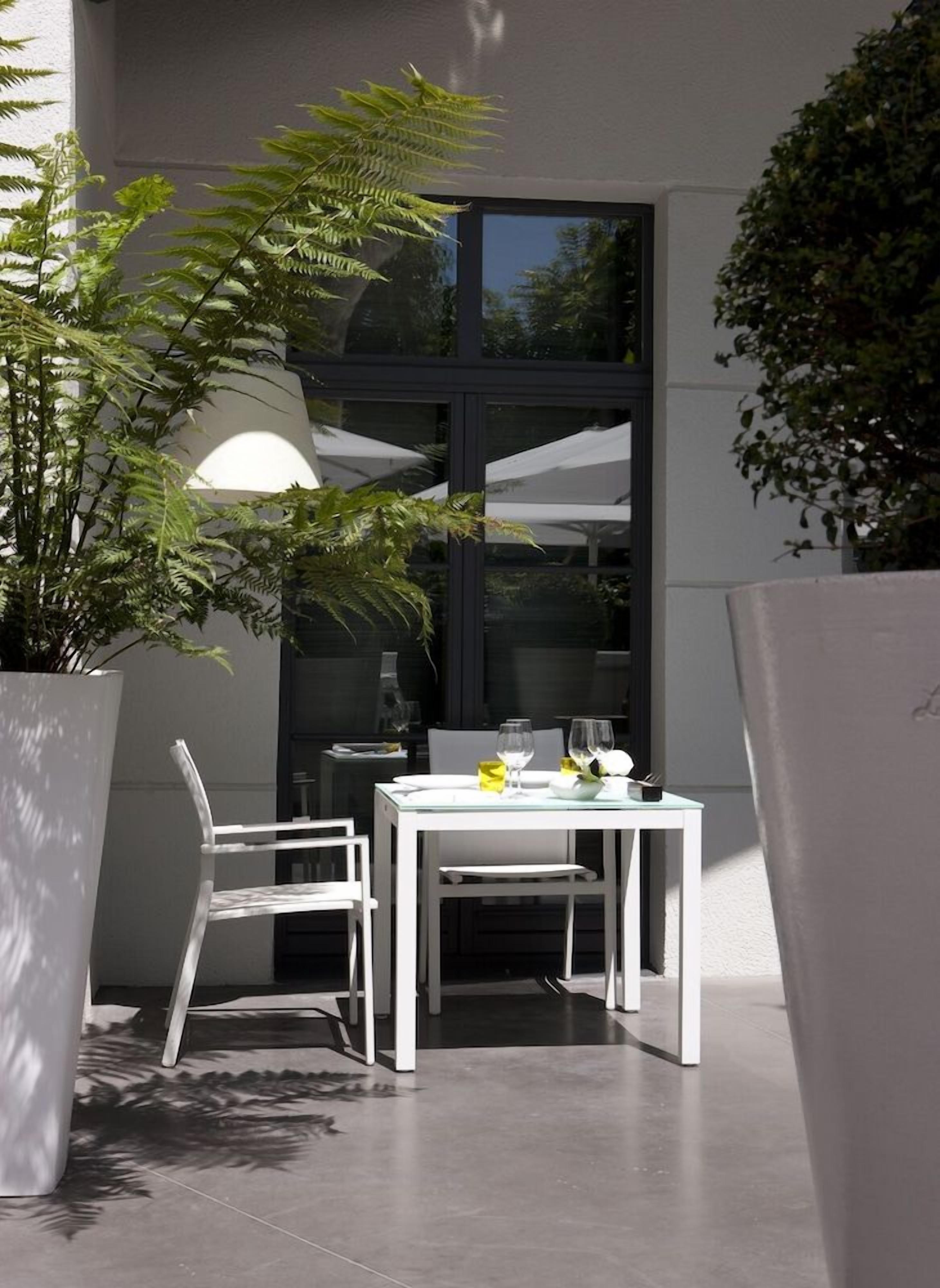 Une terrasse extérieure avec une table et des chaises, un pot de fleurs et une fenêtre donnant sur un paysage agréable.