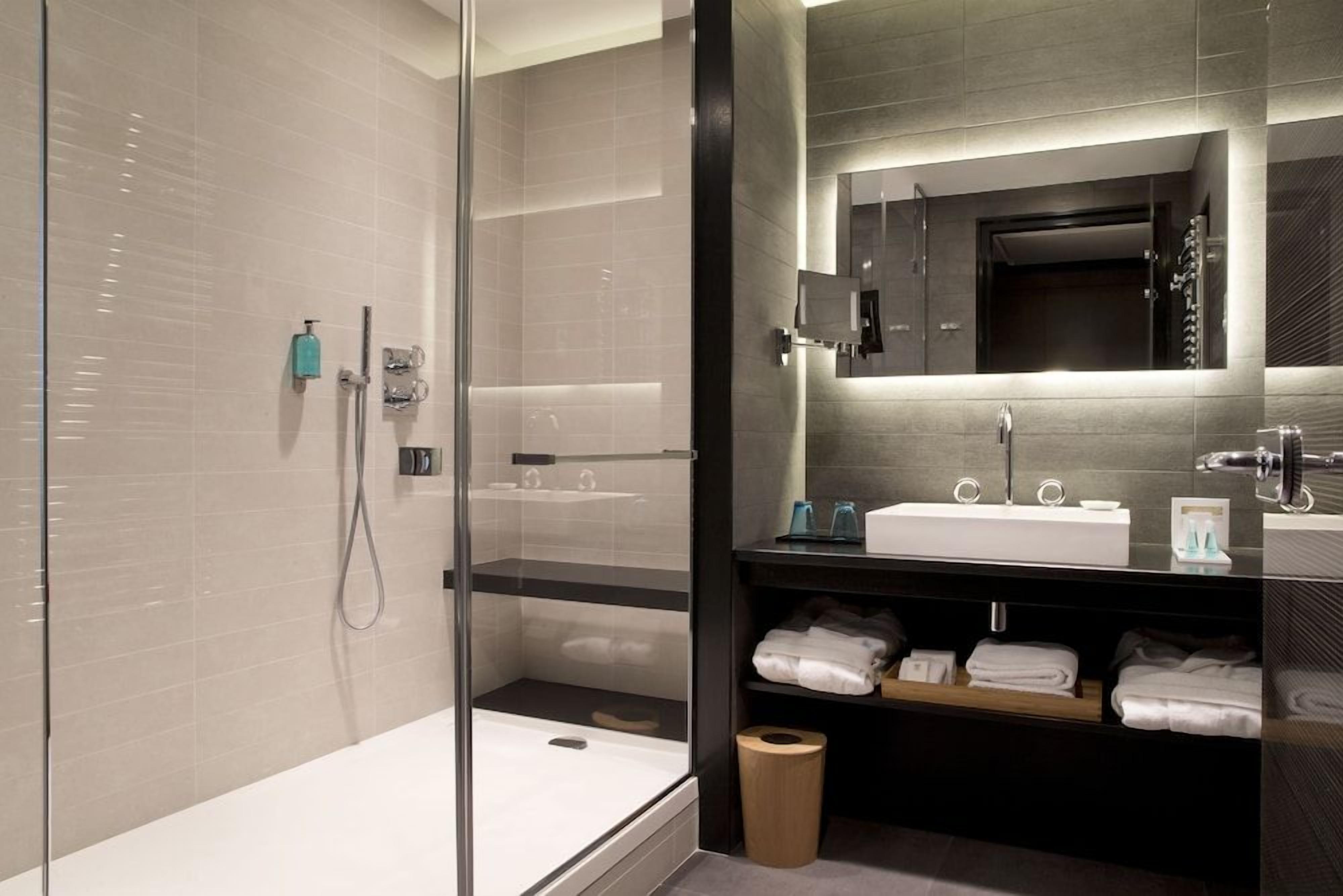 Une salle de bain moderne avec une douche à parois de verre, un meuble-lavabo avec un miroir et des serviettes soigneusement pliées sur une étagère.