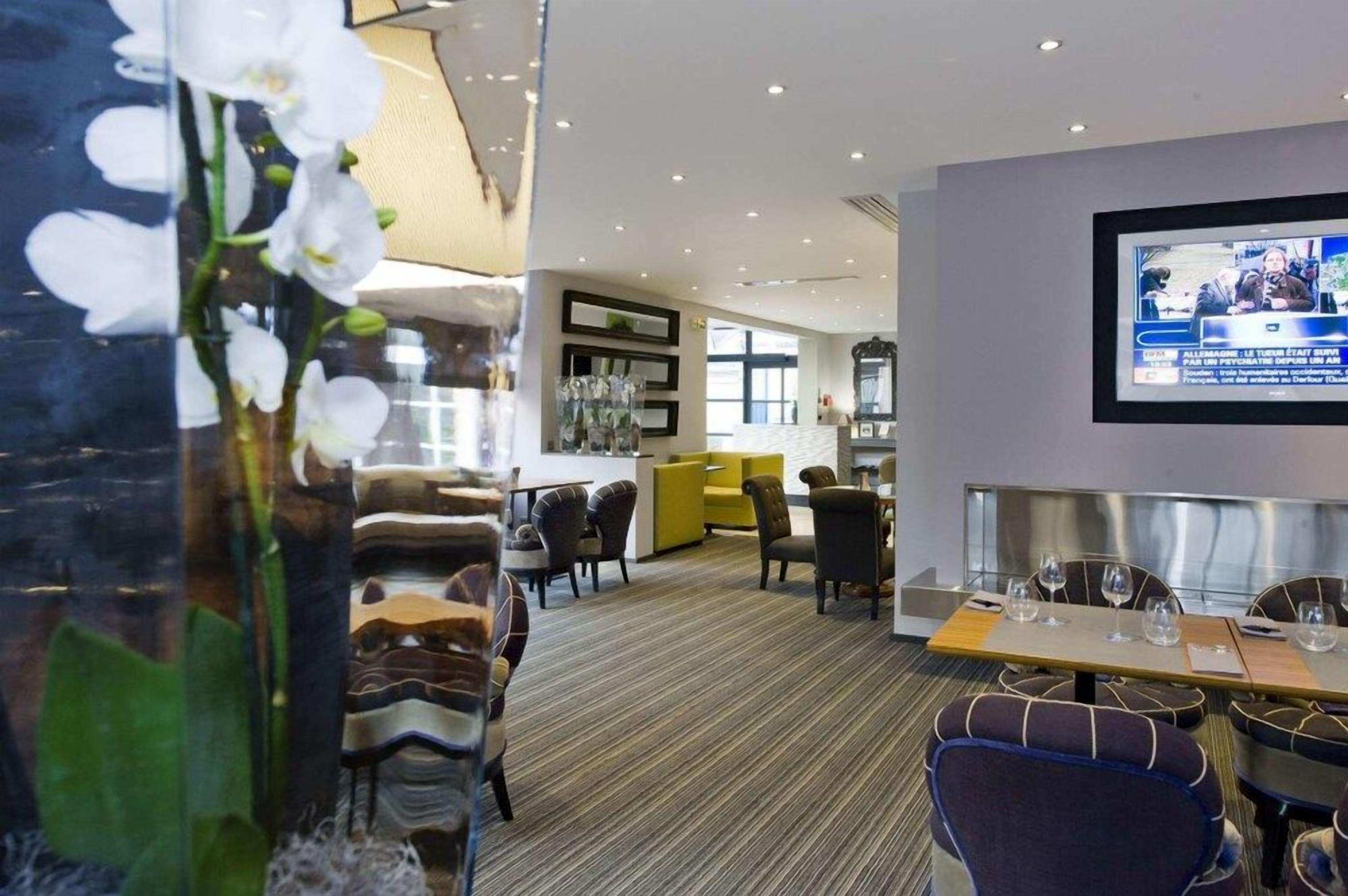 Un hall d’hôtel comprenant un espace repas, un écran de télévision et un vase décoratif orné de fleurs.