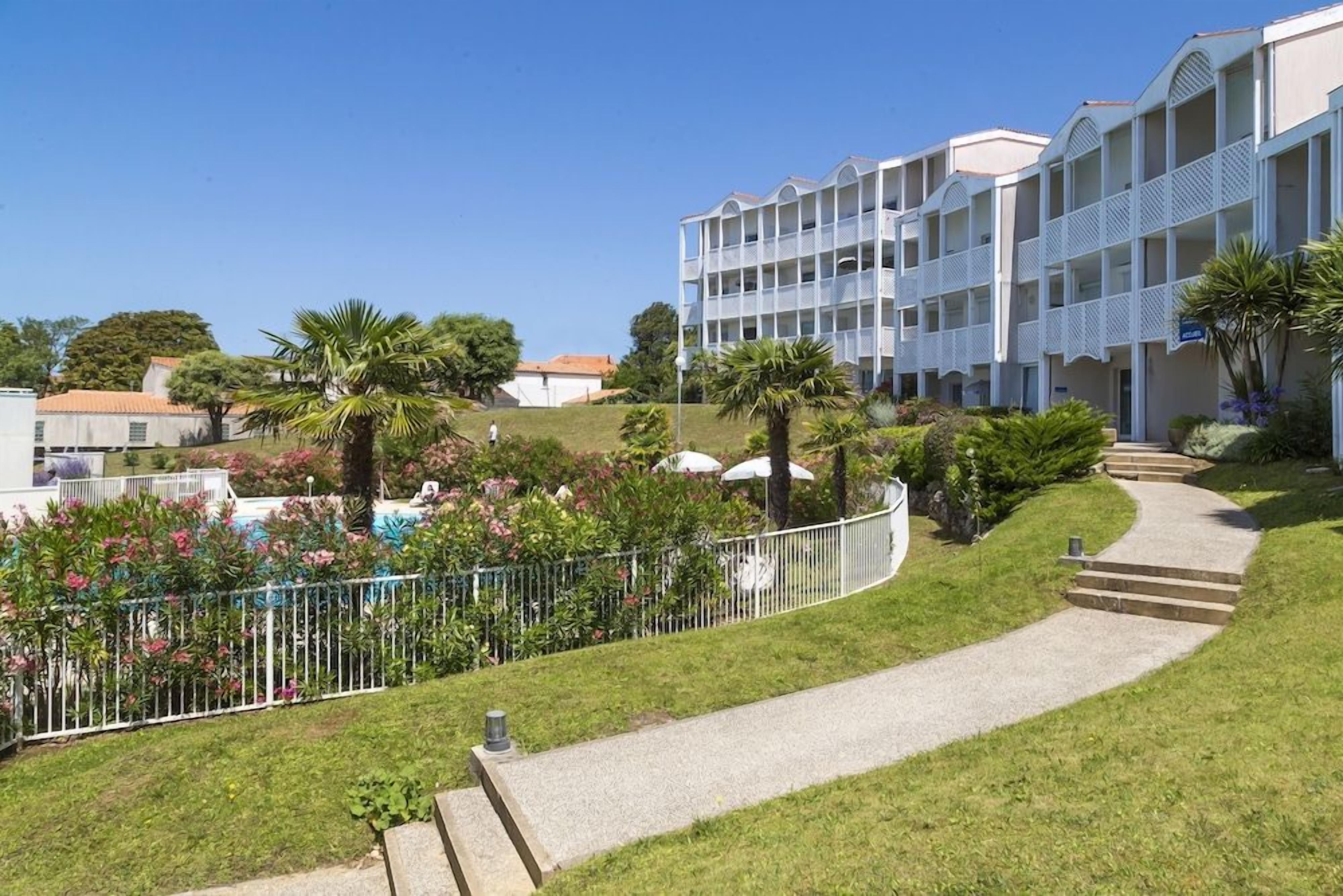 Un hôtel à plusieurs étages doté d’une cour intérieure, entouré d’une végétation luxuriante et d’un chemin sinueux.