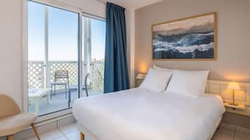 Une chambre d’hôtel avec un lit, une table de chevet avec une lampe, un tableau au mur et une porte-fenêtre coulissante donnant sur un espace extérieur avec une table et des chaises.