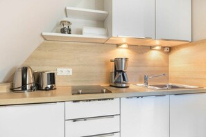 Eine moderne Küche mit Holztischplatte, einer Kaffeemaschine, einem Wasserkocher und einem Spülbecken.