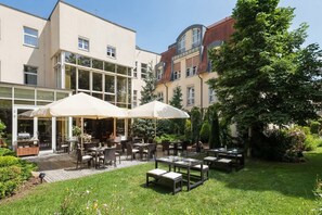 An outdoor seating area with tables and chairs, a buffet cart, and a glass-enclosed building with multiple windows.