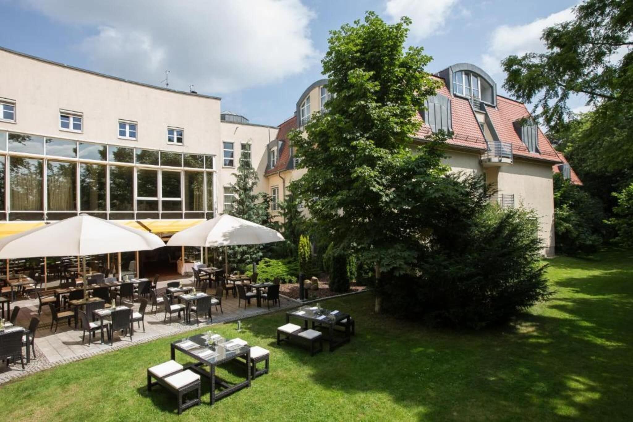 Ein Außenbereich zum Essen mit Tischen und Stühlen, umgeben von einem gepflegten Rasen und einem Gebäude mit großen Fenstern.