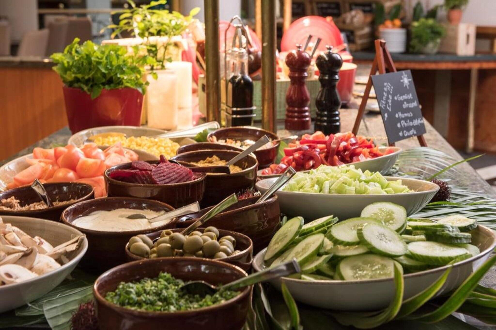 A buffet with various food options including vegetables, meats, and dips.