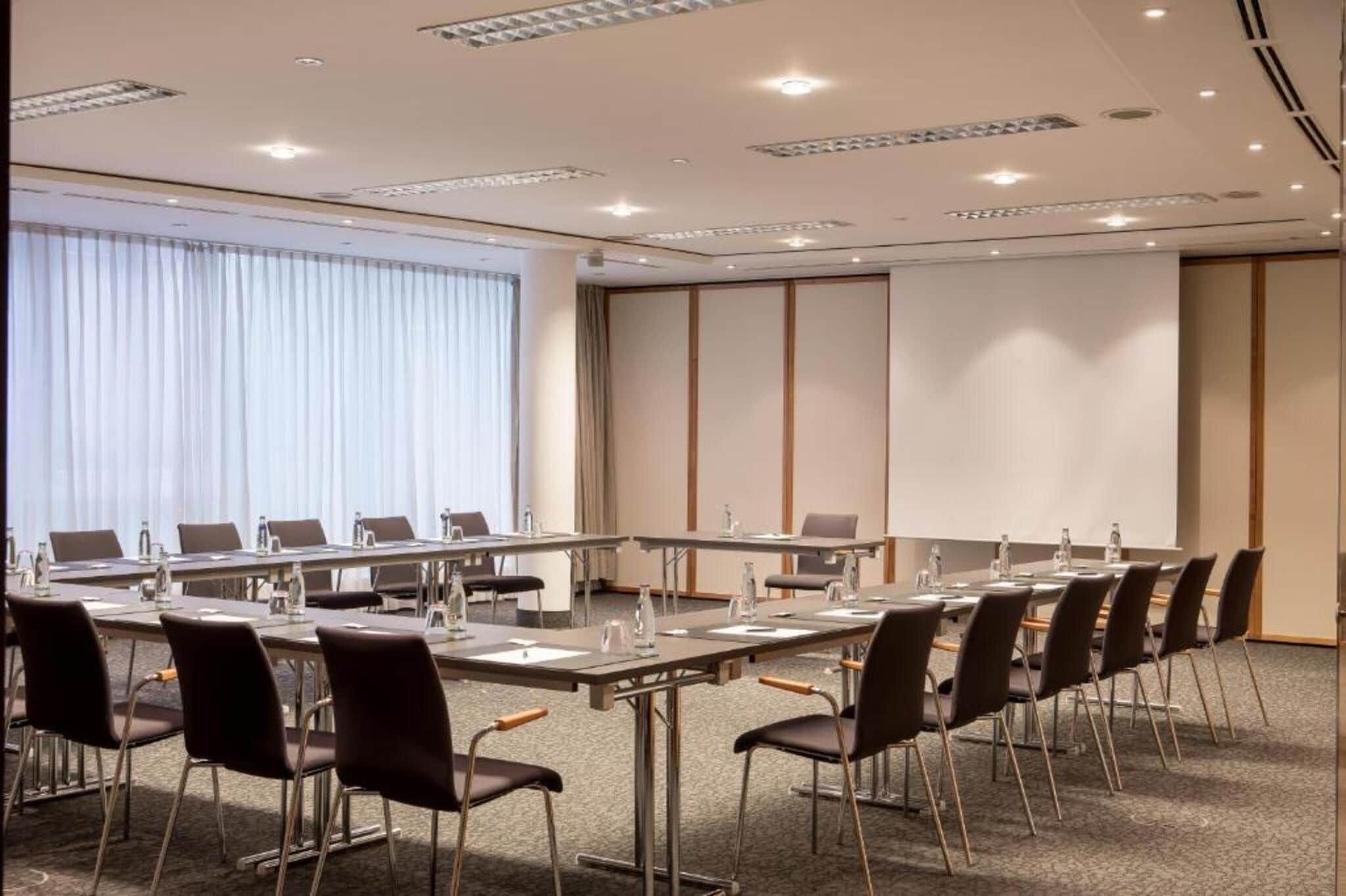 Ein Konferenzraum mit einem langen Tisch, Stühlen und einem großen Fenster mit Vorhängen.