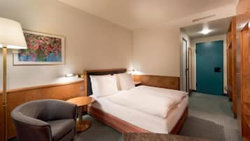 Une chambre d’hôtel avec un lit, une chaise, une petite table, un tableau au mur et une porte.