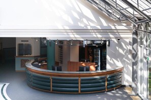 Un intérieur moderne avec un espace salon aux lignes courbes, un comptoir d’accueil et une cloison en verre.