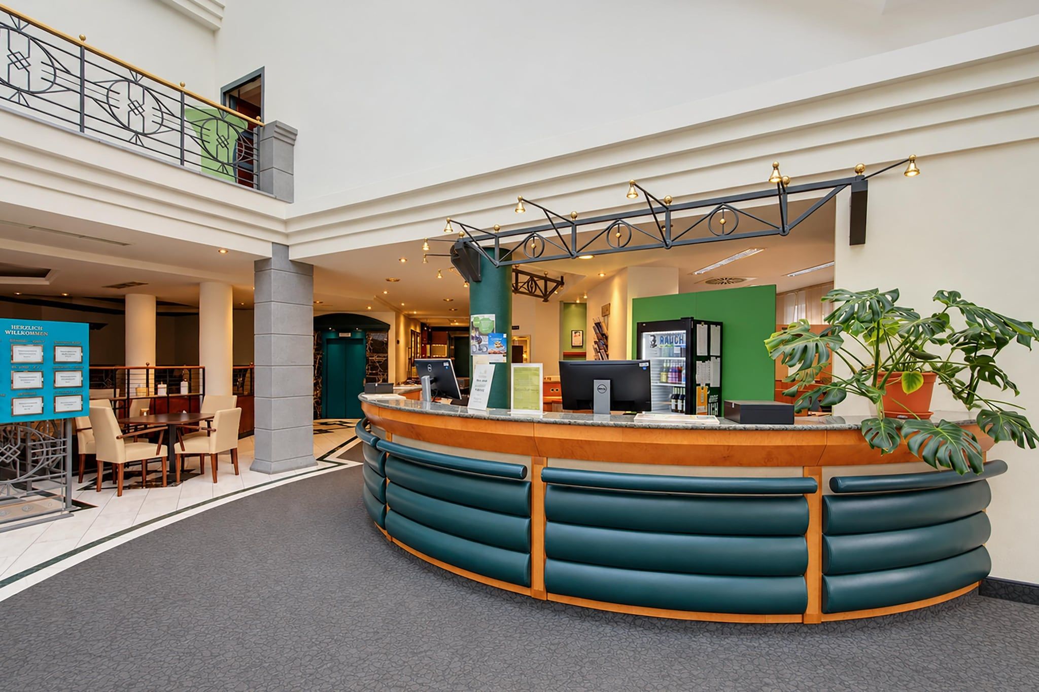 Un'area reception con un bancone curvo, una zona salotto con poltrone e una parete verde con un cartello.