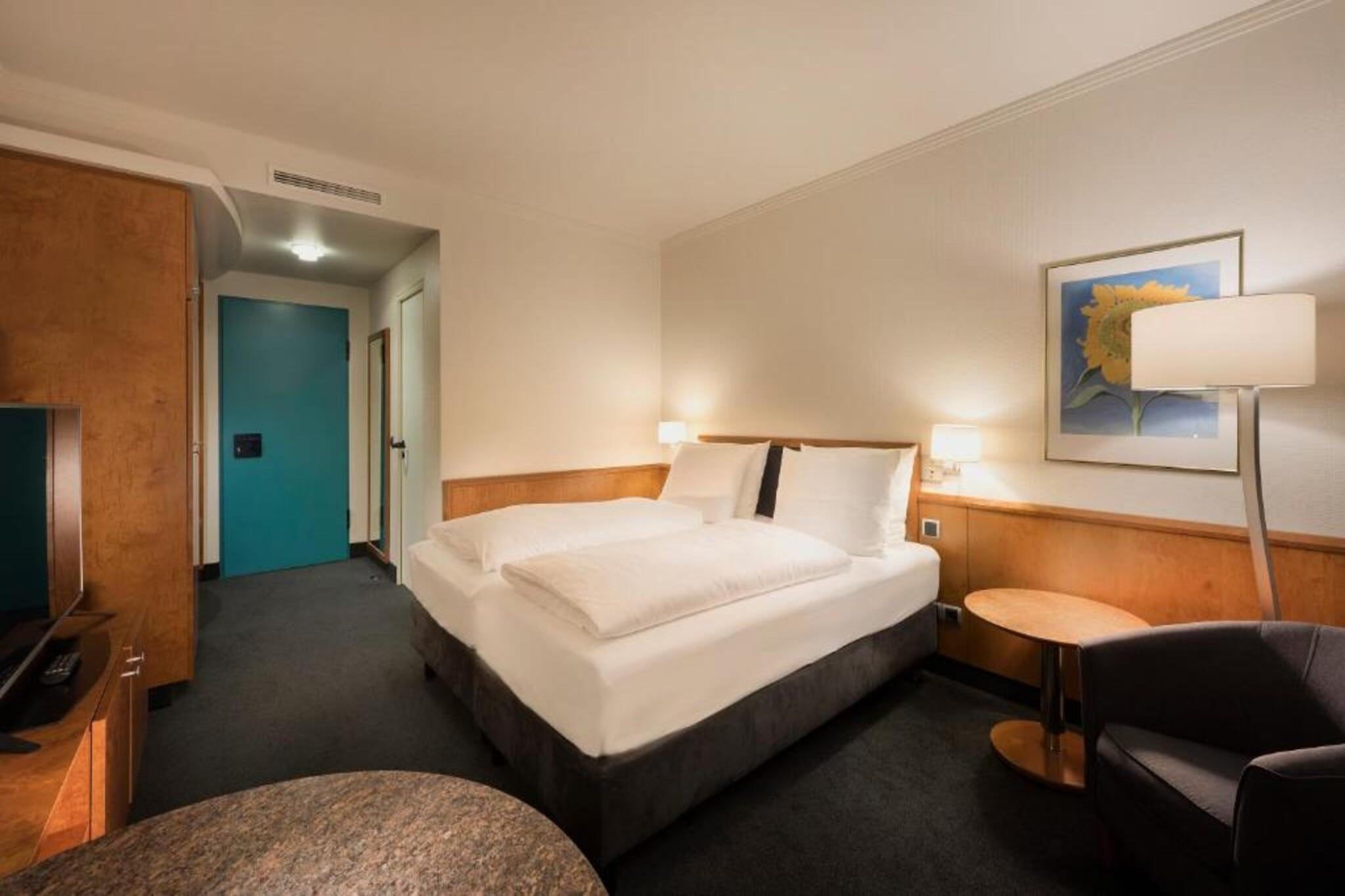 Ett hotellrum med en säng, ett skrivbord, en stol och en tavla på väggen.