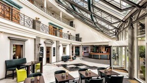 Un vestíbulo de hotel con techo de cristal, varias zonas de estar y un mostrador de recepción.