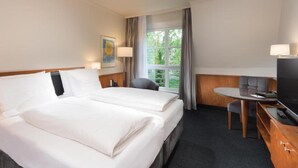 Habitación de hotel con cama doble, escritorio con televisor y ventana con cortinas.