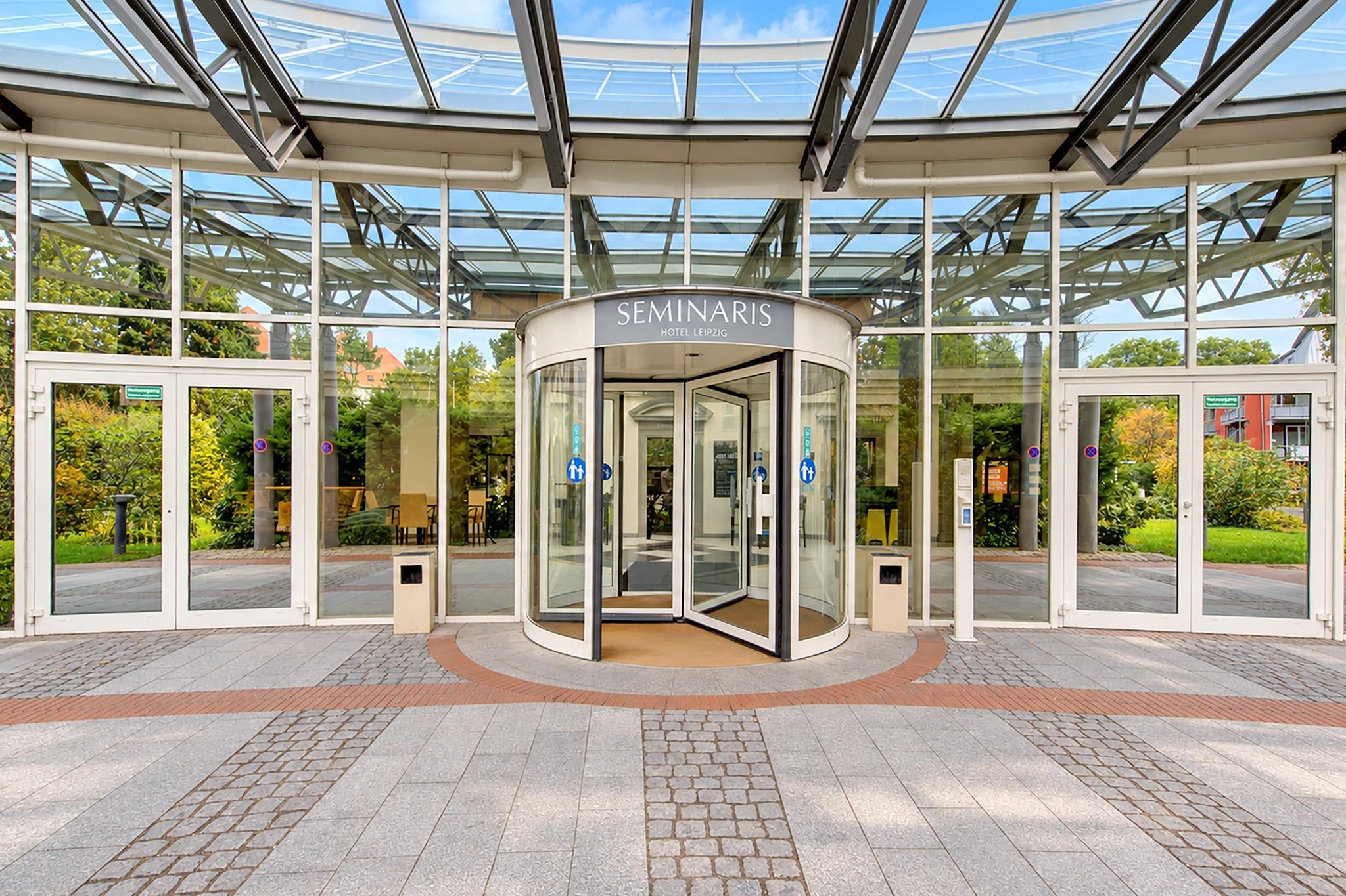 Ein moderner Hotelzugang mit einer Drehtür, Glasscheiben und freiem Blick auf die umliegende Grünfläche.