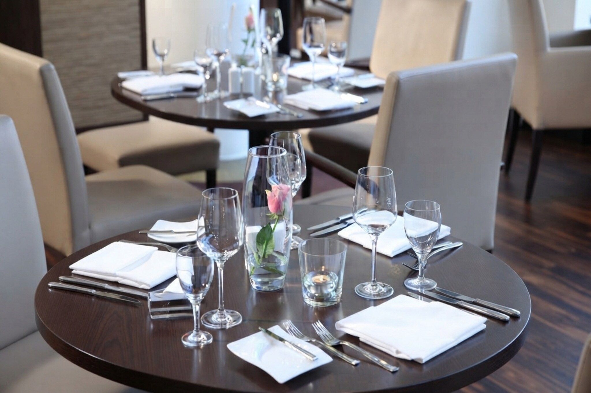Mesa de comedor preparada con varias copas de vino, vasos de agua y cubiertos, lo que sugiere una disposición formal para comer.