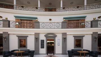 Eine mehrstöckige Hotelhalle mit einer zentralen Treppe, Sitzbereichen und Eingang zum Restaurant.